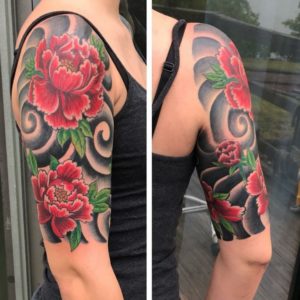 Traditional japanese red flower tattoo on beautiful woman's right arm with black swirl backround
